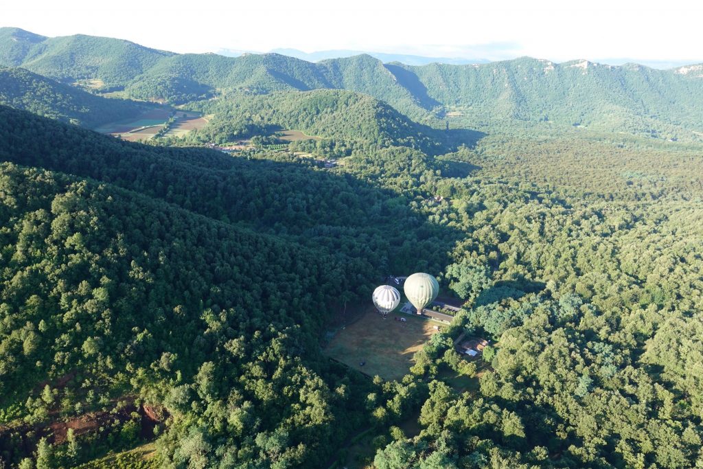 Die Umgebung des Startplatzes ist dicht grün mit Eichenwäldern bewachsen; zwei Ballone sind beim Startplatz zu sehen