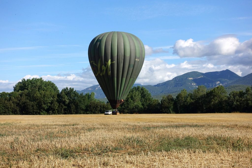 Der grüne Ballon ist am Feld gelandet, dahinter sind Bäume und Hügel zu sehen