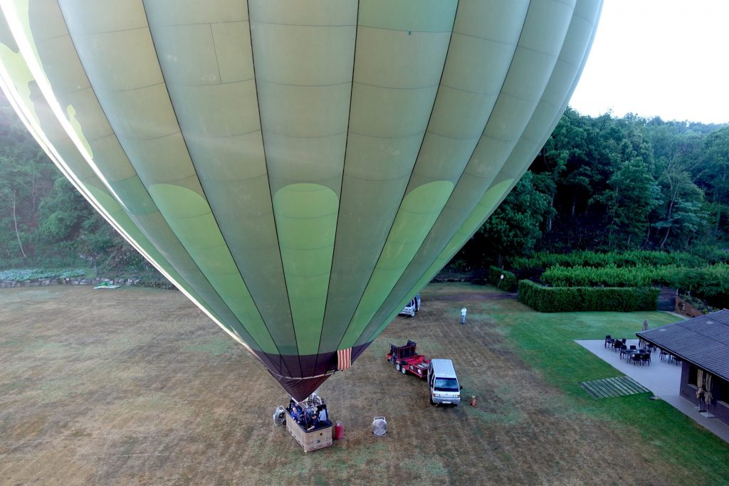aus der Luft fotografiert; ein zweiter grüner Ballon steht noch am Boden am Startplatz, daneben ein Auto mit Anhänger