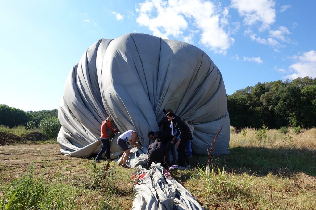 Menschen drücken den Ballon des Heißluftballons auf einem Feld zu Boden