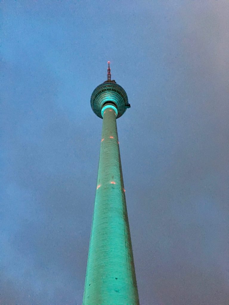Der türkis erleuchtete Berliner Fernsehturm mit seiner runden Kugel bei Einbruch der Dunkelheit und Schlechtwetter