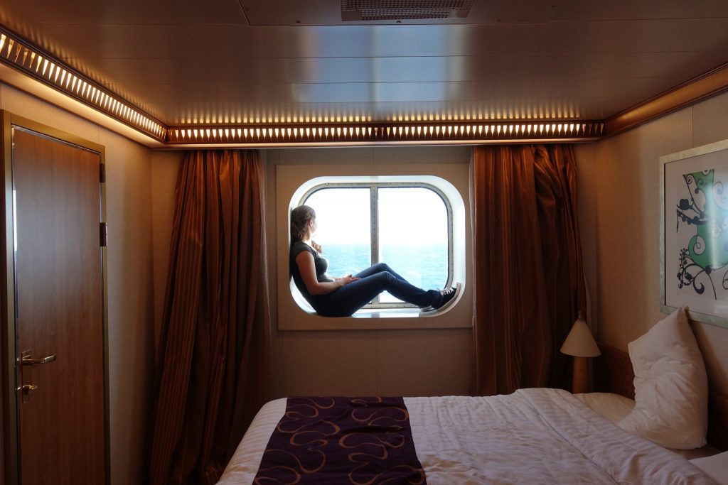 Ich sitze im Fenster der Außenkabine und schaue aufs Meer. Davor ist das Bett zu sehen.