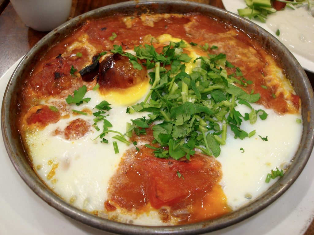Auf einem großen Teller ist das israelische Nationalgericht Shashuka zu sehen. Das Rot kommt von der Tomatensauce, das Weiß vom Ei, und das Grün ist Petersilie