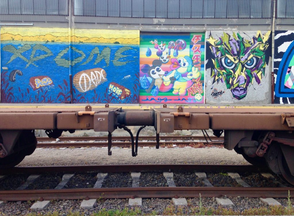 Die Wand hinter den leeren Güterzügen ist geziert mit bunten Graffitis am Mural Harbor am Industriehafen der Linz AG